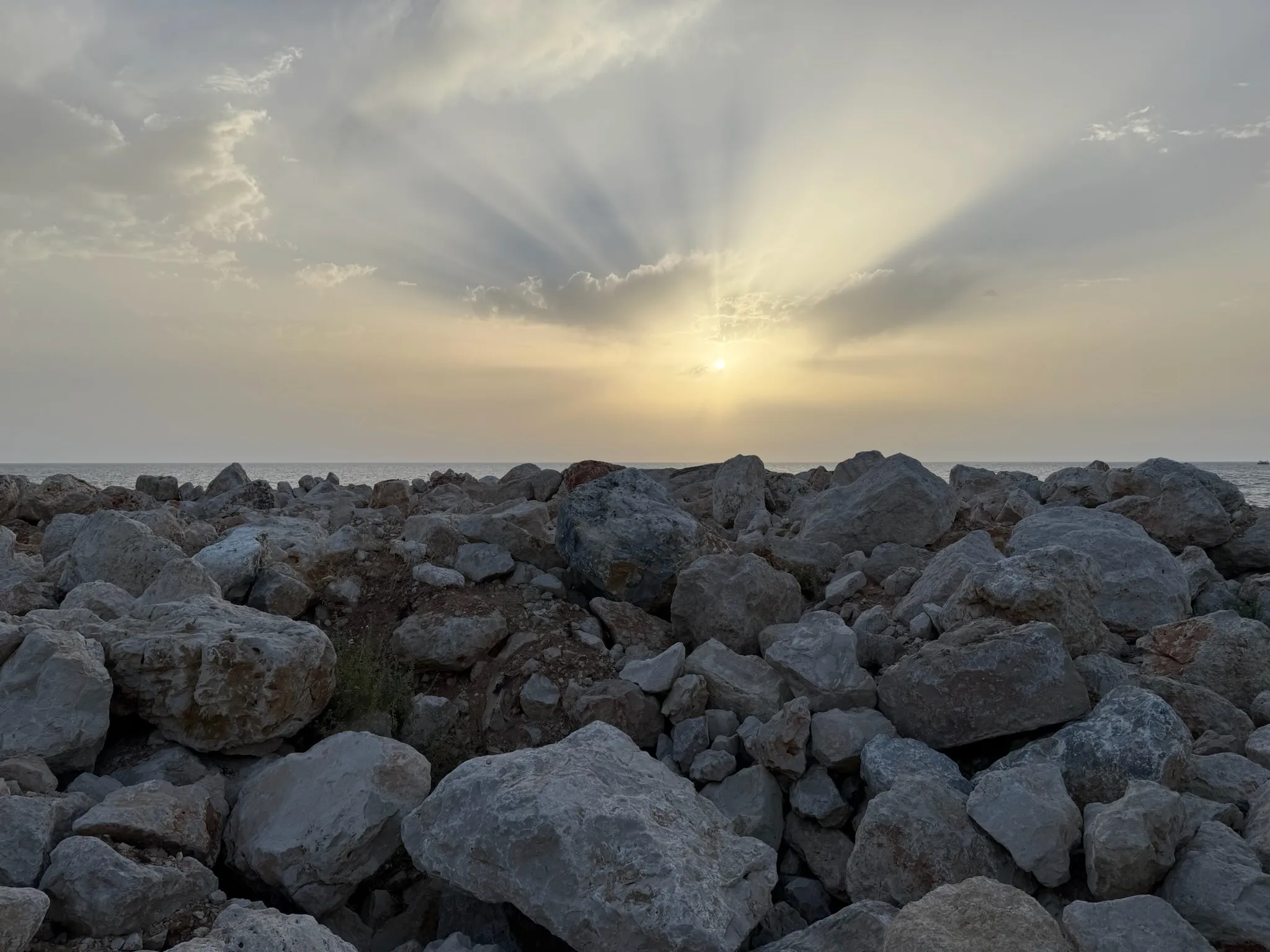 Sunrays break through cloud over a stone shoreline at dawn on the Israeli coast.